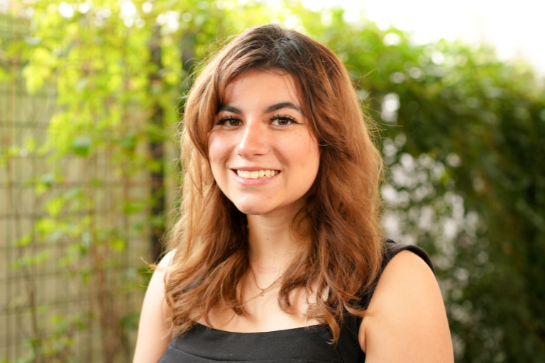 photo of a girl with reddish-orange hair, smiling in a black tank top behind a green leafy background