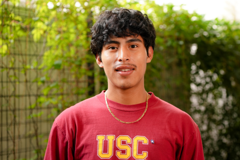 photo of a man with curly black hair wearing a USC sweater in front of a leafy background